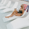 Guest relaxing on a white Forma luxury in-pool chaise lounge with matching side table on a shallow pool shelf