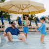 Adult relaxing on a Forma commercial in-pool lounge chair while children play on a shallow pool shelf