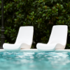 Two white Forma commercial pool edge chairs overlooking a resort-style swimming pool
