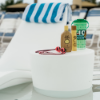Forma in-pool hospitality side table holding sunscreen, swim goggles, and a water bottle beside a pool chaise