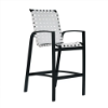 A three-quarter front view of a high-top Skyline commercial outdoor bar chair featuring a black powder-coated aluminum frame, armrests, a lower footrest bar, and white vinyl straps in a cross-weave pattern.