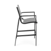 Side profile view of a high-top patio bar chair showing a starlight black aluminum frame with dark metallic platinum sling fabric and integrated footrest.