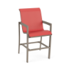 Three-quarter perspective view of a tall outdoor bar height arm chair with a beige Satin Amber aluminum frame, footrests, and a vibrant coral pink Straw Mat textured sling.