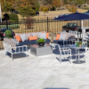 An outdoor patio setup featuring white Sonoma cushioned armchairs and deep seating lounge furniture arranged around a small metal bistro table and coffee table under a large patio umbrella.