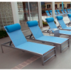 A row of silver aluminum Urban chaise lounges lined up along a commercial pool deck, fitted with light blue sling seating and matching blue bolster headrest pillows.