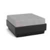 A front three-quarter view studio product shot of a square commercial outdoor ottoman featuring a dark Black Granite Marine Grade Polymer (MGP) platform base topped with a thick light gray upholstered cushion.