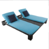 High angle perspective view of a two-person outdoor chaise lounge with dark gray woven resin wicker, light blue full-length cushions, and navy patterned square accent pillows.