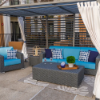 Outdoor lounge patio setup under a slatted gazebo featuring a dark gray wicker sofa and armchair with turquoise cushions, a matching rectangular wicker coffee table, and patterned accent pillows.