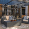 Commercial outdoor patio setup under a steel pergola featuring a dark gray wicker loveseat and matching armchair with off-white cushions, accent pillows, and a rectangular wicker coffee table.
