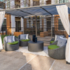 Outdoor patio seating arrangement under a metal pergola featuring four dark gray resin wicker barrel chairs with green seat cushions and patterned throw pillows, arranged around a dark circular coffee table.