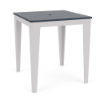 Three-quarter perspective view of a 36-inch square MGP outdoor bar-height table featuring a navy blue slatted tabletop with a centered umbrella hole, set on a clean white frame and tapered legs.