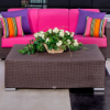 A three-seat commercial outdoor sofa with a Java chocolate brown woven resin wicker frame and hot pink cushions, styled behind a matching rectangular wicker coffee table topped with a flower arrangement.