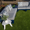 A small white triangular 20-inch marine-grade polymer (MGP) modern outdoor side table holding a potted plant in the foreground, positioned next to a dark navy blue outdoor modular sectional with grey cushions on artificial turf.