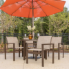 A outdoor patio dining set featuring four brown aluminum stackable sling club chairs arranged around a matching patio table with a flower vase, all shaded under a large orange patio umbrella on a concrete patio.