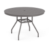 Eye-level perspective view of a 42-inch round Sundance commercial aluminum outdoor dining table in Titanium Gray powder coat, showcasing splayed legs, umbrella cross-bracing, and an aluminum tabletop perforated with a uniform square cube grid pattern and middle umbrella hole.