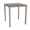 A square outdoor bar-height patio table featuring a smooth grey slatted MGP top with a center umbrella hole, supported by a Satin Amber beige aluminum frame.