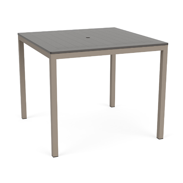 A 48-inch square bar-height patio table featuring a neutral grey slatted MGP tabletop with an umbrella hole, supported by a Satin Amber beige aluminum base.