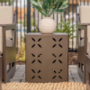 A textured espresso square side table styled outdoors between two matching lounge chairs on a patio, holding a round decorative vase with greenery.